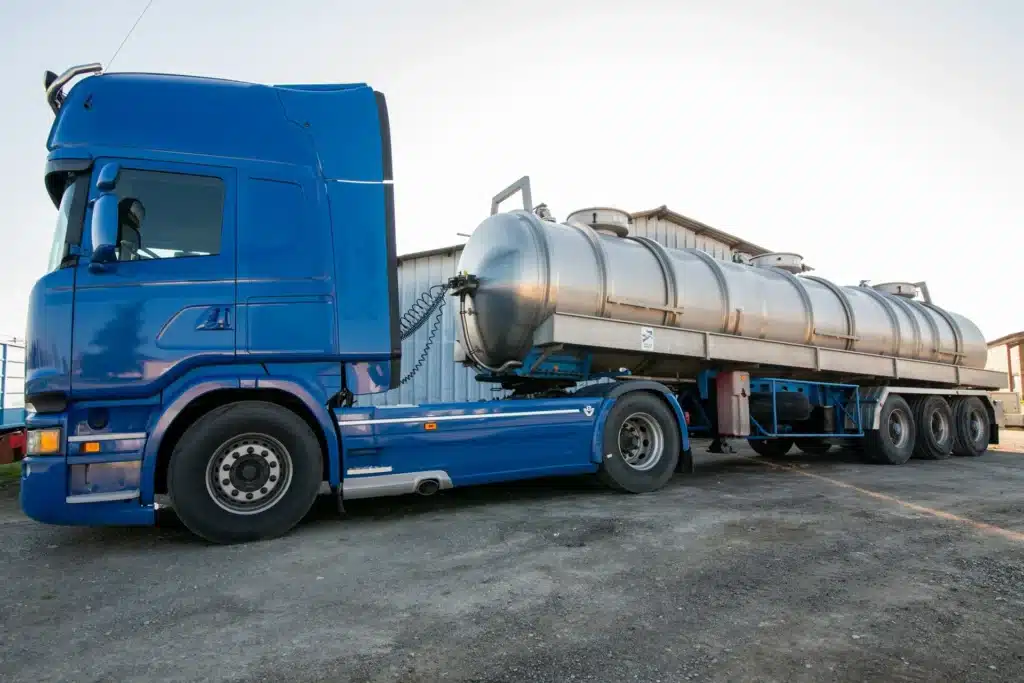 Camion Citerne Bleu et Semi-Remorque Inox Industriel Semi-remorque citerne en inox et camion bleu stationnés sur un terrain industriel en plein jour.