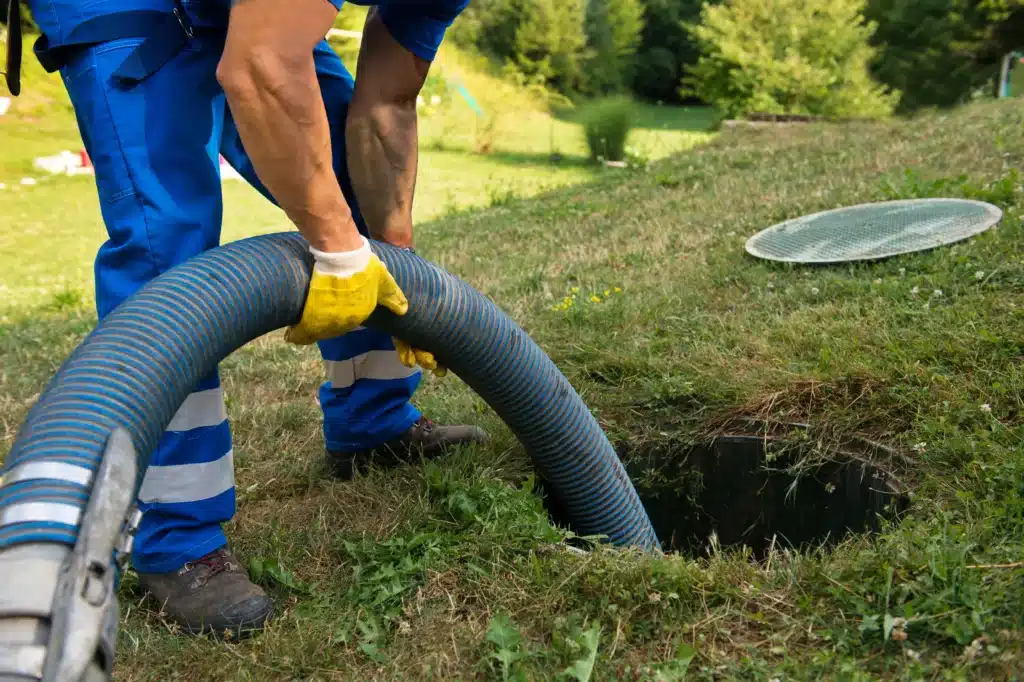 Vidange fosse septique : entretien et pompage professionnel Professionnel insérant un tuyau de pompage bleu dans une fosse septique ouverte pour une vidange.